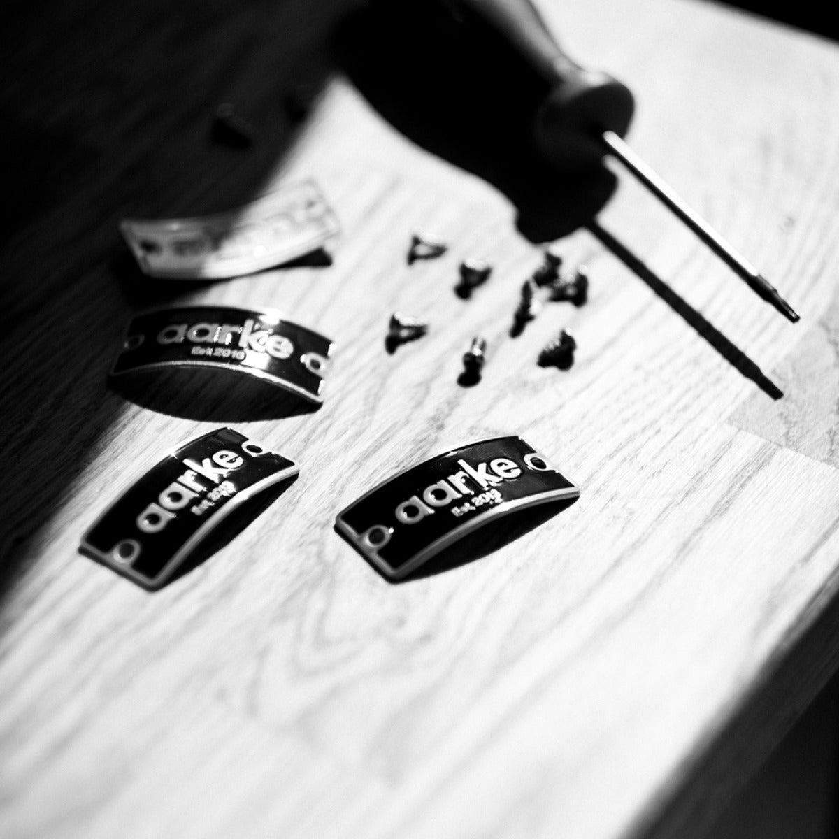 Engraved Aarke name plates beside a screwdriver and screws.