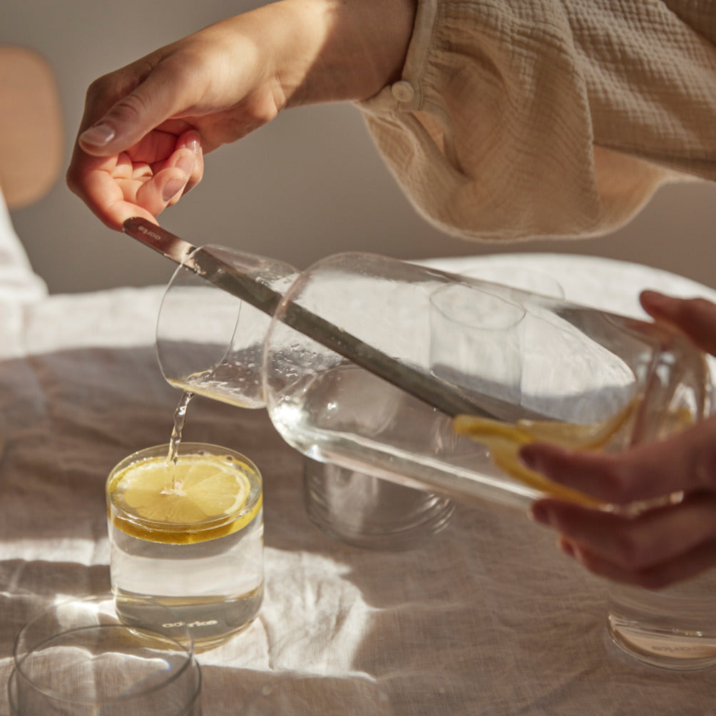 A person pours water from the Aarke Nesting Carafe into a glass.