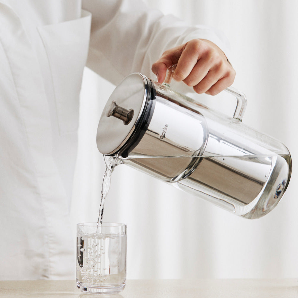 Someone pours a glass of water into a glass from the Aarke Purifier