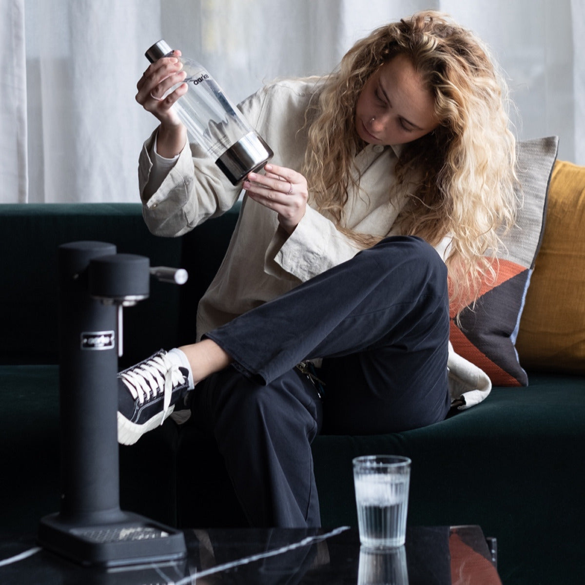 A woman sitting on a couch examines the Aarke PET Bottle.