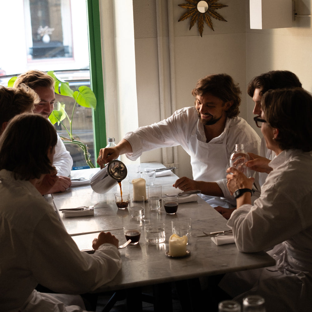 People in a dining setting with one person pouring a drink.