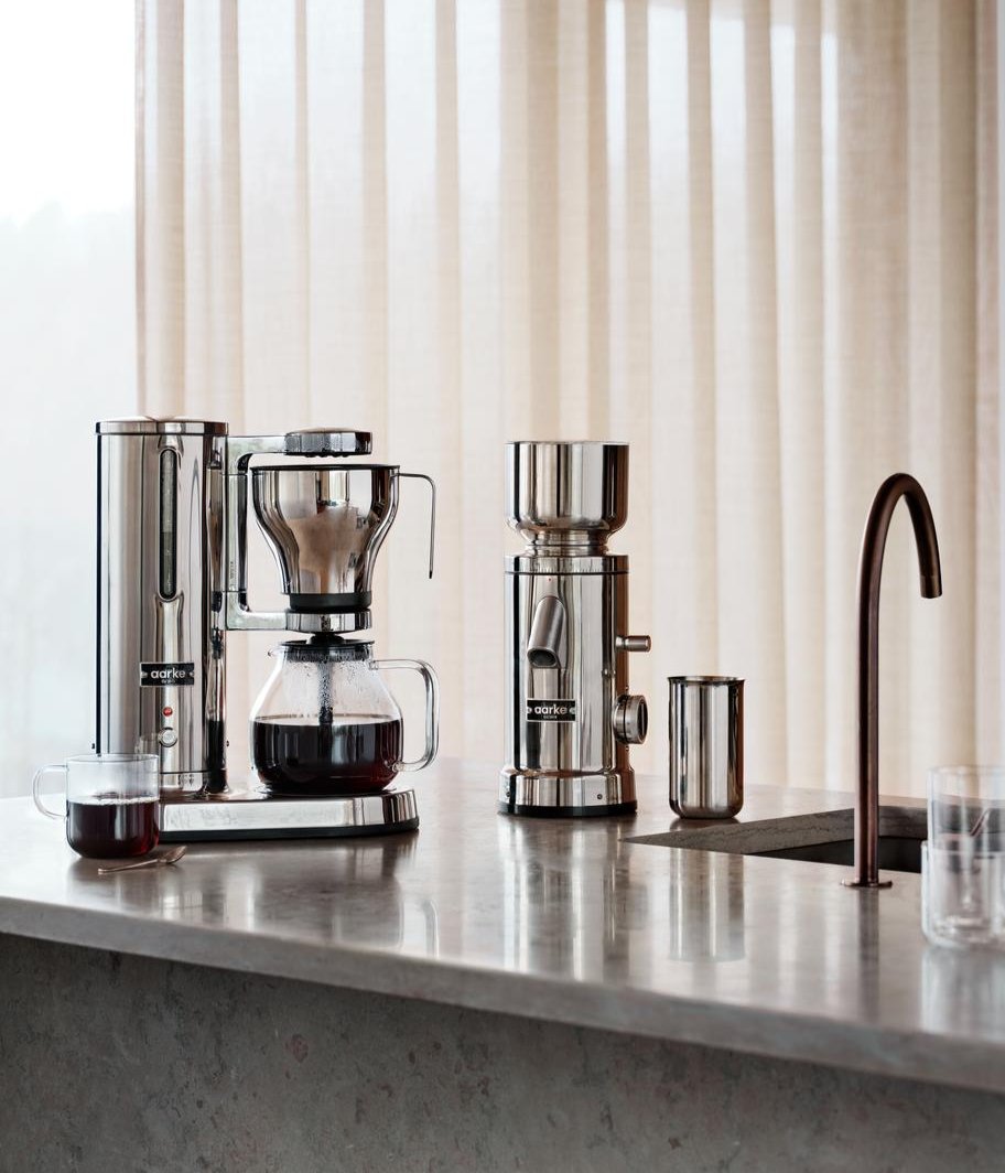 aarke coffee maker and coffee grinder standing on kitchenisland in a setting of marble stone. 