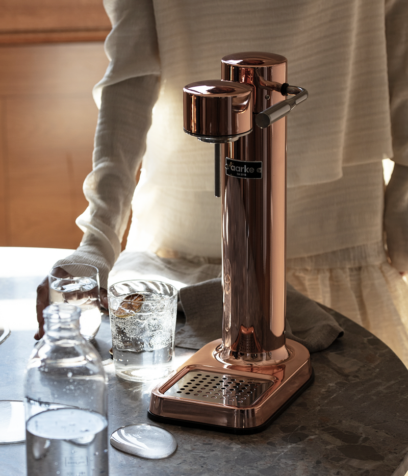 Aarke Carbonator 3 in copper finish on a kitchen counter with glasses of sparkling water.