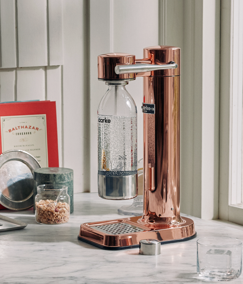 Aarke Carbonator 3 in copper finish on a marble countertop, carbonating water in an Aarke PET bottle.