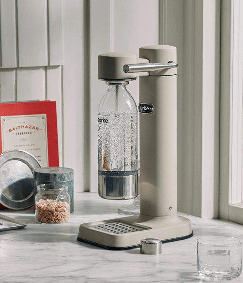 Aarke Carbonator 3 in sand finish on a marble countertop, carbonating water in an Aarke PET bottle.