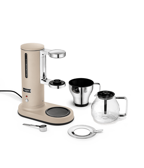 Aarke sand-colored automatic pour-over coffee maker with stainless steel filter cone, glass coffee carafe and measuring scoop – premium Scandinavian drip coffee brewer.