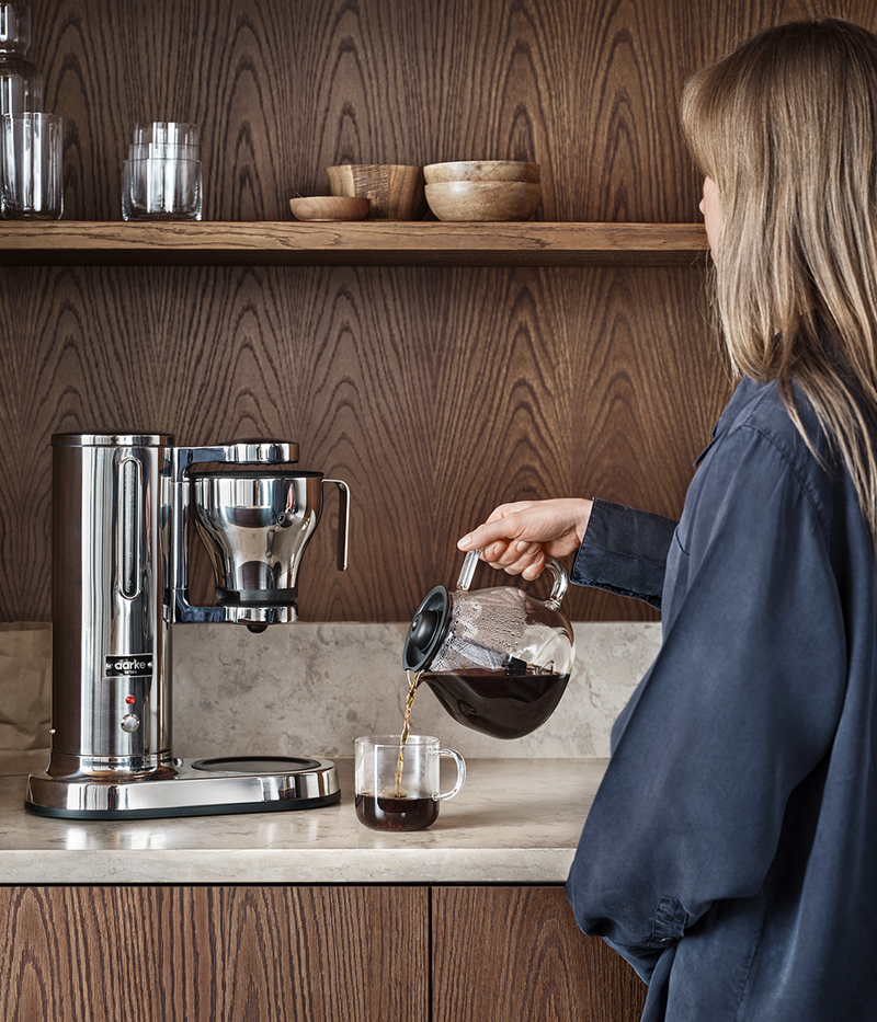 girl pouring coffee in coffee mug. aarke coffee maker standing in the background on the kitchen counter top