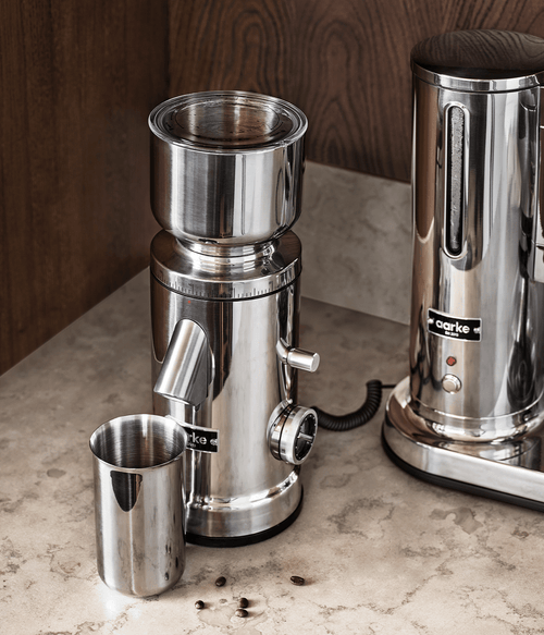 Aarke Coffee Grinder and Coffee Maker on marble counter with coffee container and scattered beans.