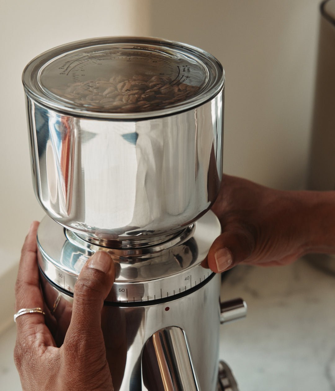 Hands adjusting the grind size on the Aarke stainless steel coffee grinder filled with coffee beans.