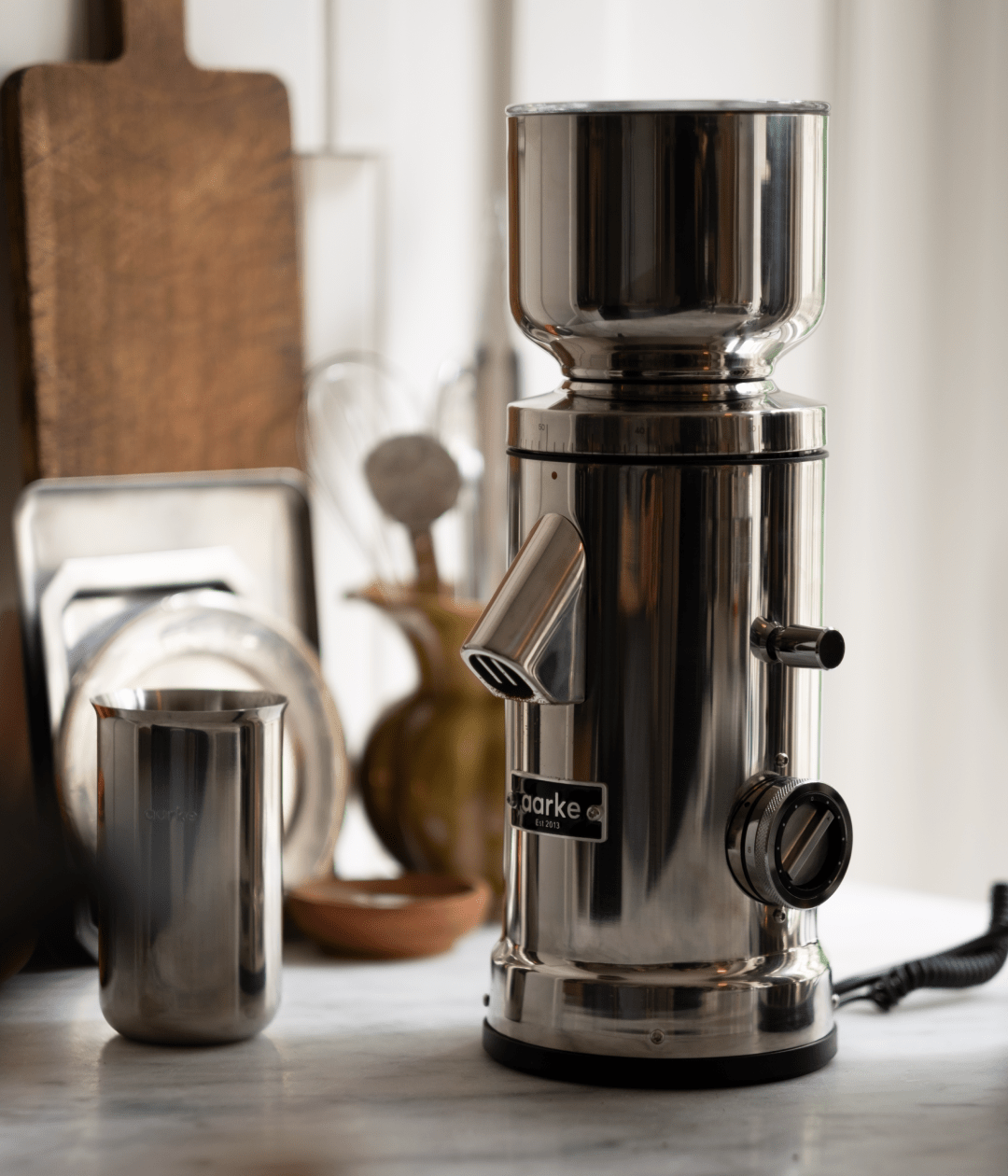 Aarke stainless steel coffee grinder on a kitchen counter with a matching stainless steel container beside it.