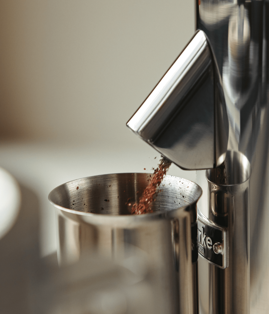 Ground coffee dispensing from the Aarke stainless steel coffee grinder into a metal container.
