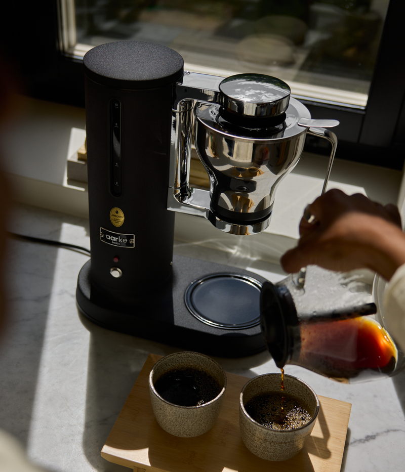 Person pouring coffee from the Aarke coffee maker Matte Black into two cups on a marble surface.