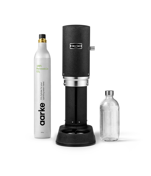 Front view of Aarke Carbonator Pro in matte black, accompanied by a CO2 gas cylinder and a glass bottle filled with sparkling water.