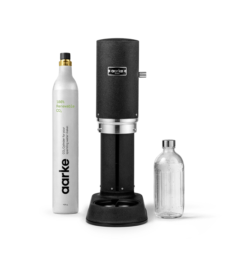 Front view of Aarke Carbonator Pro in matte black, accompanied by a CO2 gas cylinder and a glass bottle filled with sparkling water.