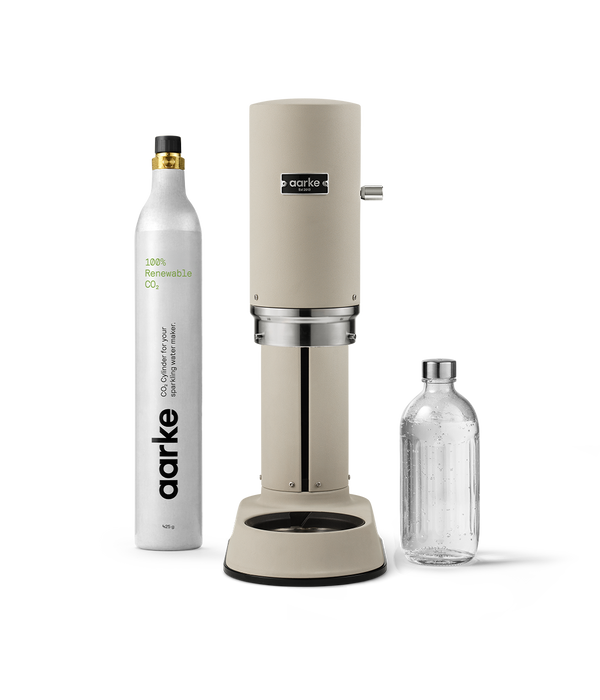 Front view of Aarke Carbonator Pro Sand, accompanied by a CO2 gas cylinder and a glass bottle filled with sparkling water.