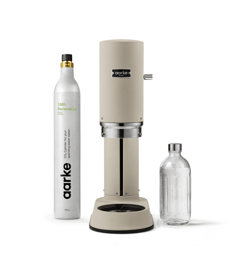 Front view of Aarke Carbonator Pro Sand, accompanied by a CO2 gas cylinder and a glass bottle filled with sparkling water.