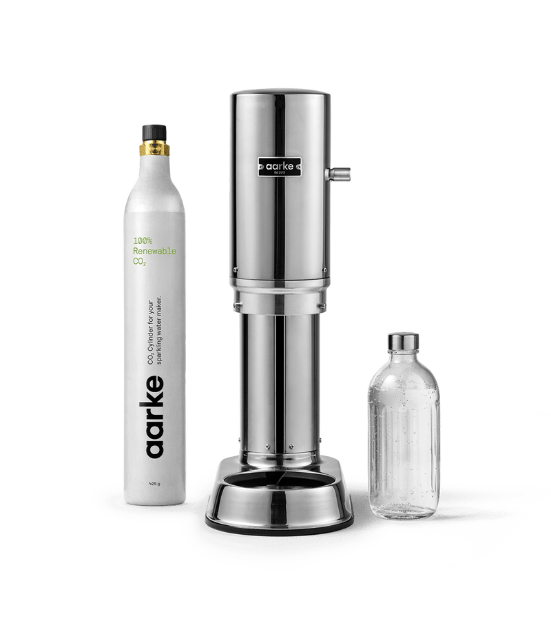 Front view of Aarke Carbonator Pro Steel, accompanied by a CO2 gas cylinder and a glass bottle filled with sparkling water.