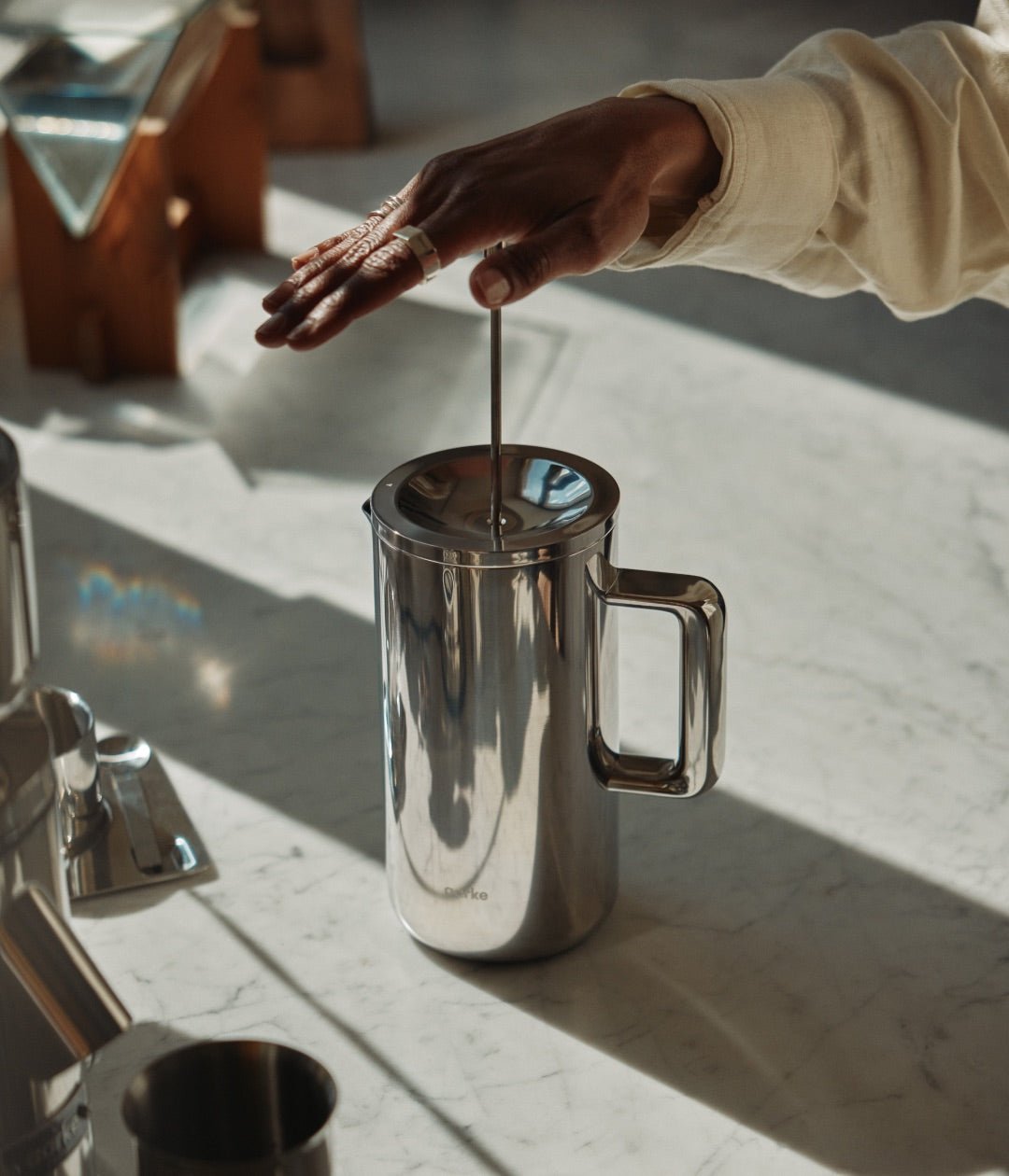 Hand pressing Aarke stainless steel French Press plunger on marble countertop.