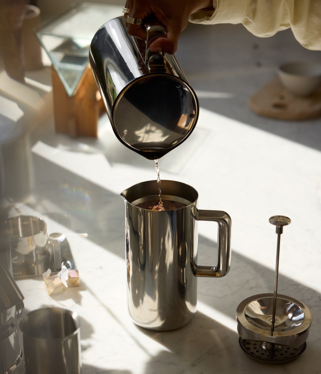 Person pouring hot water into Aarke stainless steel French Press using the Aarke Kettle.