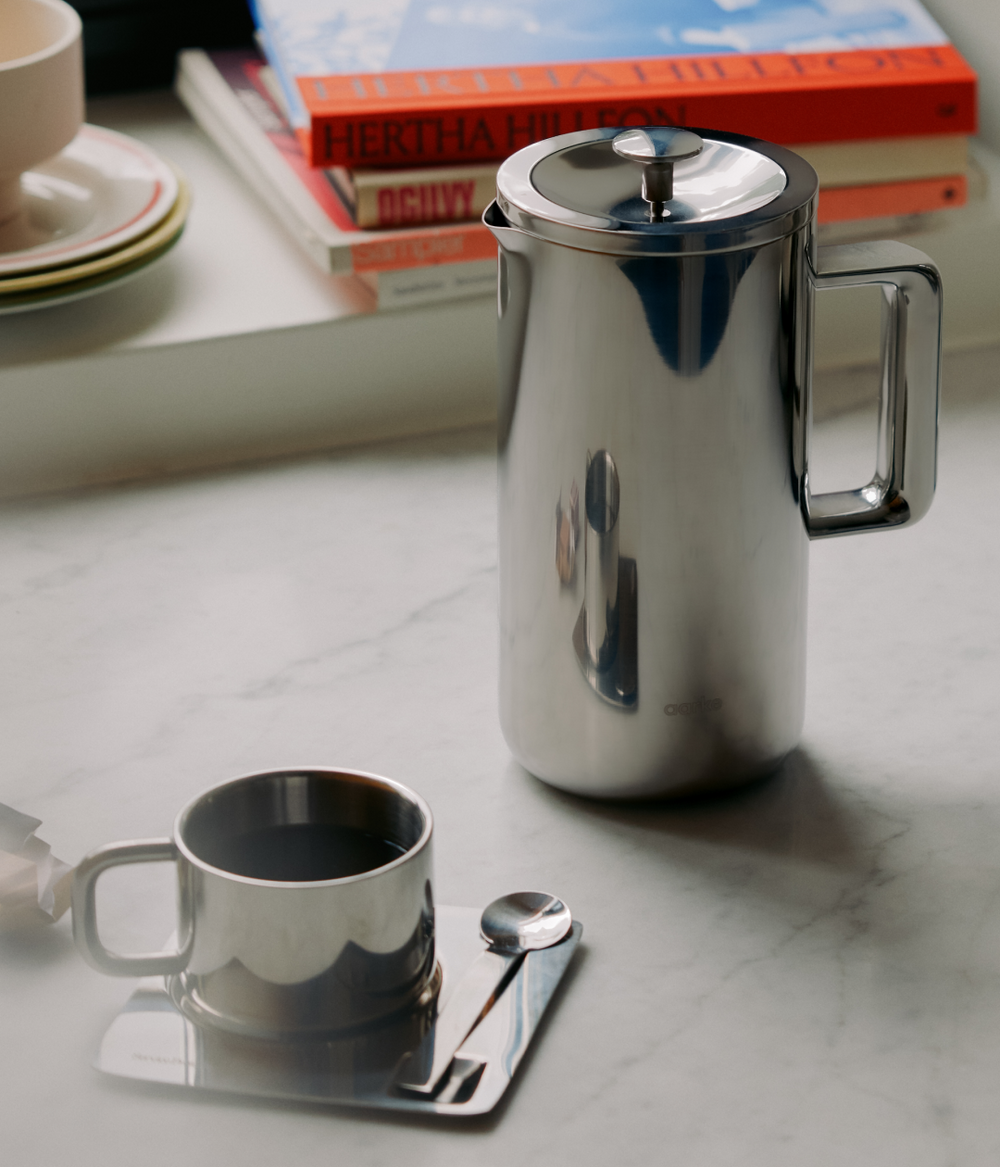 Aarke Stainless steel coffee press on a marble surface with a cup and books in the background
