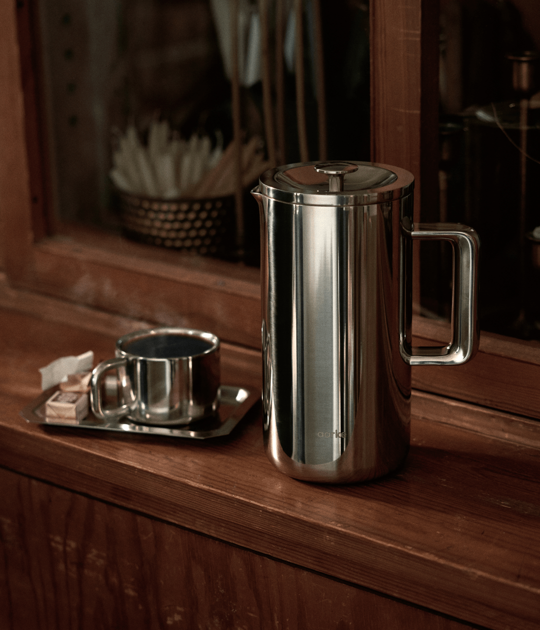 Aarke French Press stainless steel with cup on wooden counter for premium coffee moments.