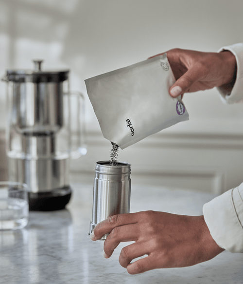 Close-up of person refilling Aarke filter cartridge with Enriched granules from refill bag on kitchen counter.