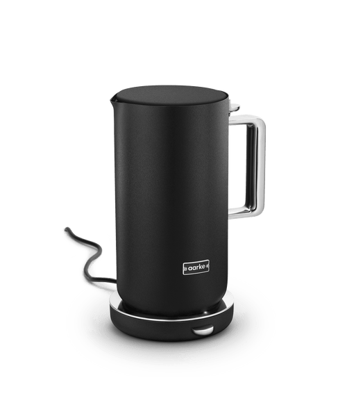 Aarke Kettle in Matte Black placed on its base with power cord visible in the background.