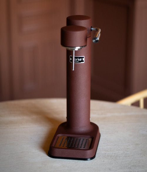 Aarke Carbonator 3 in Burgundy standing alone on a round, light-colored table with matching interior tones.