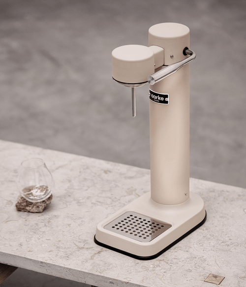 Aarke Carbonator 3 in sand finish on a stone table with a glass of sparkling water.