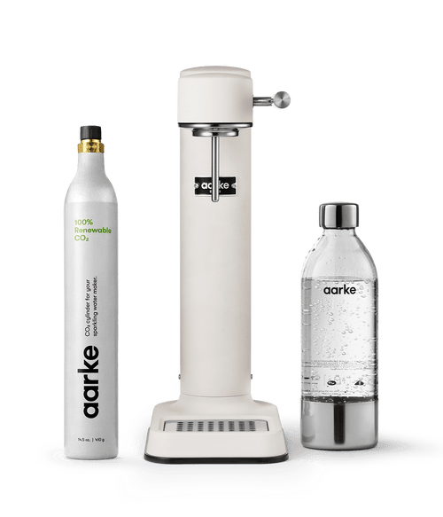 Aarke Carbonator 3 in Matte White displayed with a 100% renewable CO2 cylinder next to a filled PET water bottle.