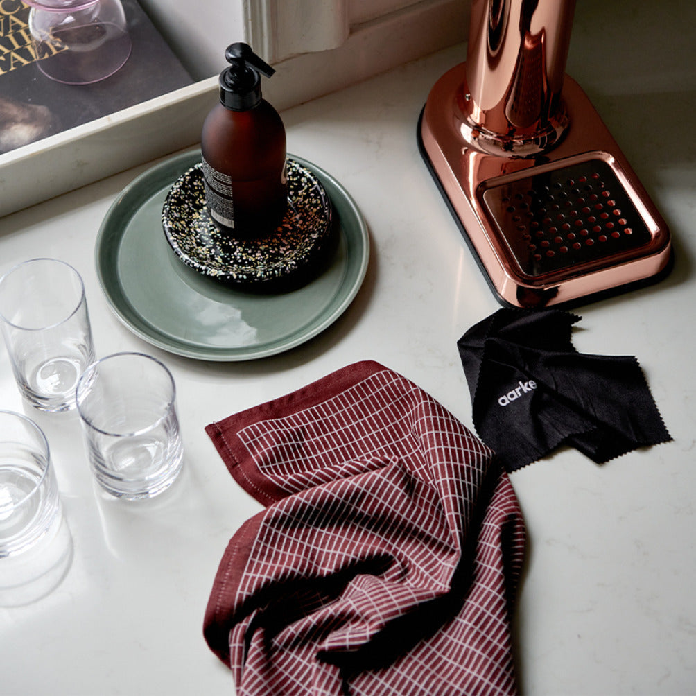 A table showing a cleaning cloth, polishing cloth, and base of the Aarke Carbonator 3 in Copper.