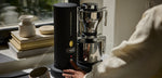 Aarke matte black coffee maker in use, modern stainless steel design on kitchen counter.