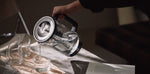 Aarke Purifier glass and stainless steel water filter pitcher pouring filtered water into a glass.