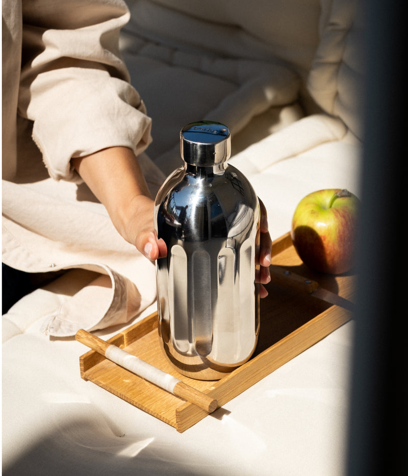 Person holding the Aarke To-Go Bottle on a wooden tray with an apple and glass in the background.