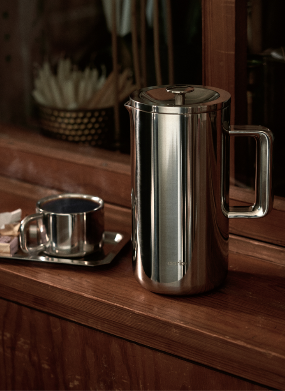 Aarke French Press stainless steel with cup on wooden counter for premium coffee moments.