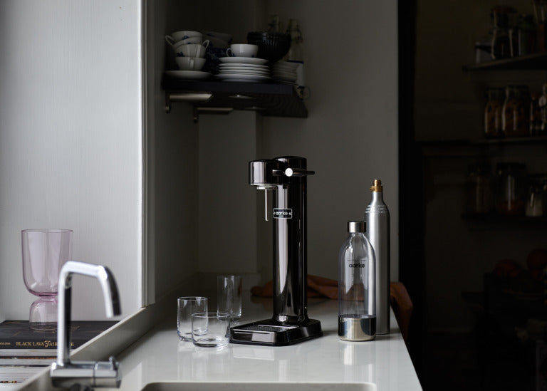 The Aarke Carbonator 3 in Black Chrome pictured beside a PET Bottle and cylinder of Aarke CO2.