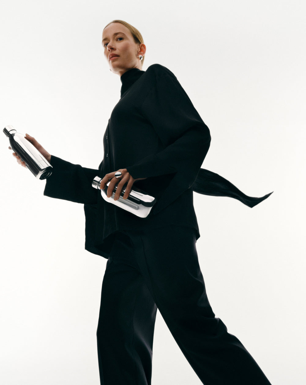 Person wearing a black outfit holding two Aarke To-go stainless steel bottles against a white background.