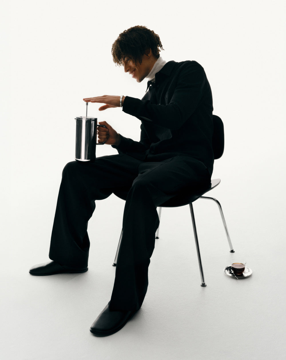 Person in a suit sitting on a chair using the Aarke French Coffee Press.