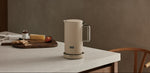 AARKE Kettle Sand electric kettle on a kitchen counter with stainless steel handle, styled in a warm Scandinavian kitchen setting.
