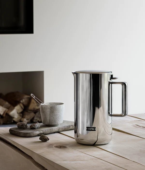 The Aarke kettle in stainless steel placed on a wooden table next to a cup and dried ingredients.