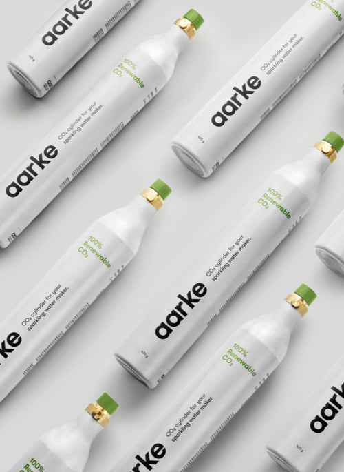 Multiple Aarke CO₂ cylinders with green caps arranged diagonally on a light grey background, labeled 100% Renewable CO₂.