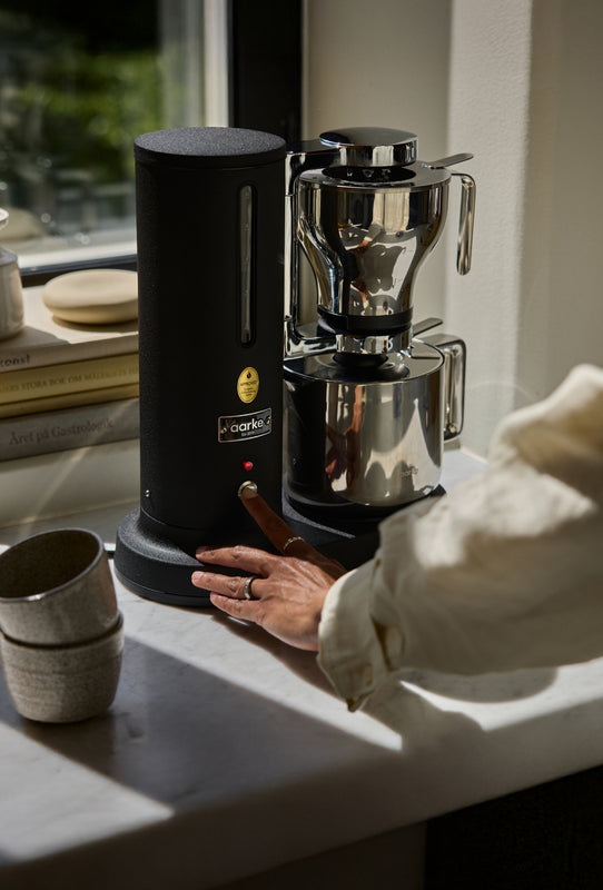 Aarke matte black coffee maker in use, modern stainless steel design on kitchen counter.