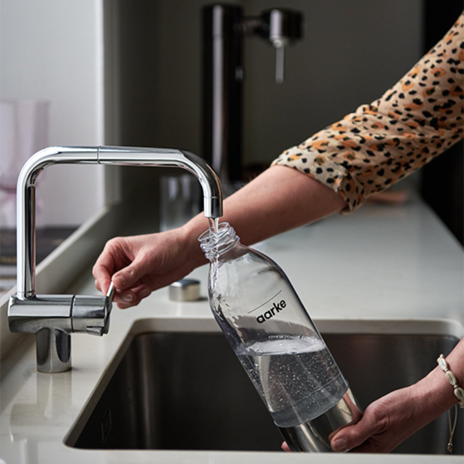 A person filling an Aarke PET Bottle with water in a kitchen sink.