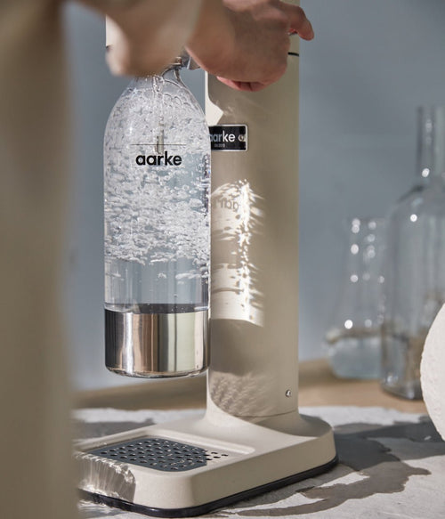Hand pressing lever on Aarke Carbonator 3 in Sand while carbonating water.