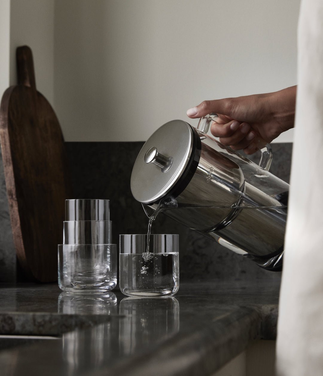 A person pouring water from an Aarke water purifier into a glass on a dark kitchen countertop.