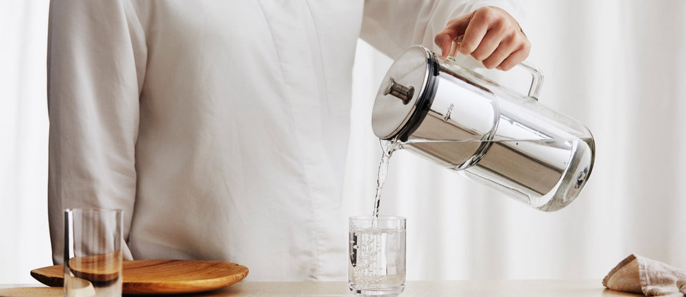 A person pours water into a glass from the Aarke Water Purifier Pitcher.