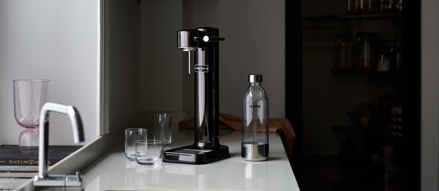 The Aarke Carbonator 3 in Black Chrome pictured beside a PET Bottle and cylinder of Aarke CO2.