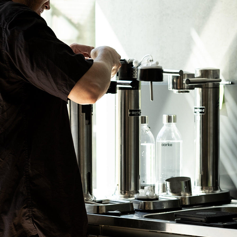 Person making coffee using a professional espresso machine with clear containers labeled 'barista' in the background.