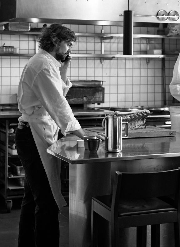 Person in a kitchen wearing an apron, standing at a counter with a french press and bowl.