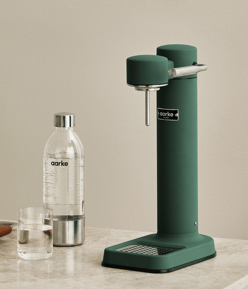 Aarke Carbonator 3 in Heritage Green with a sparkling water bottle and glass on a marble kitchen countertop.
